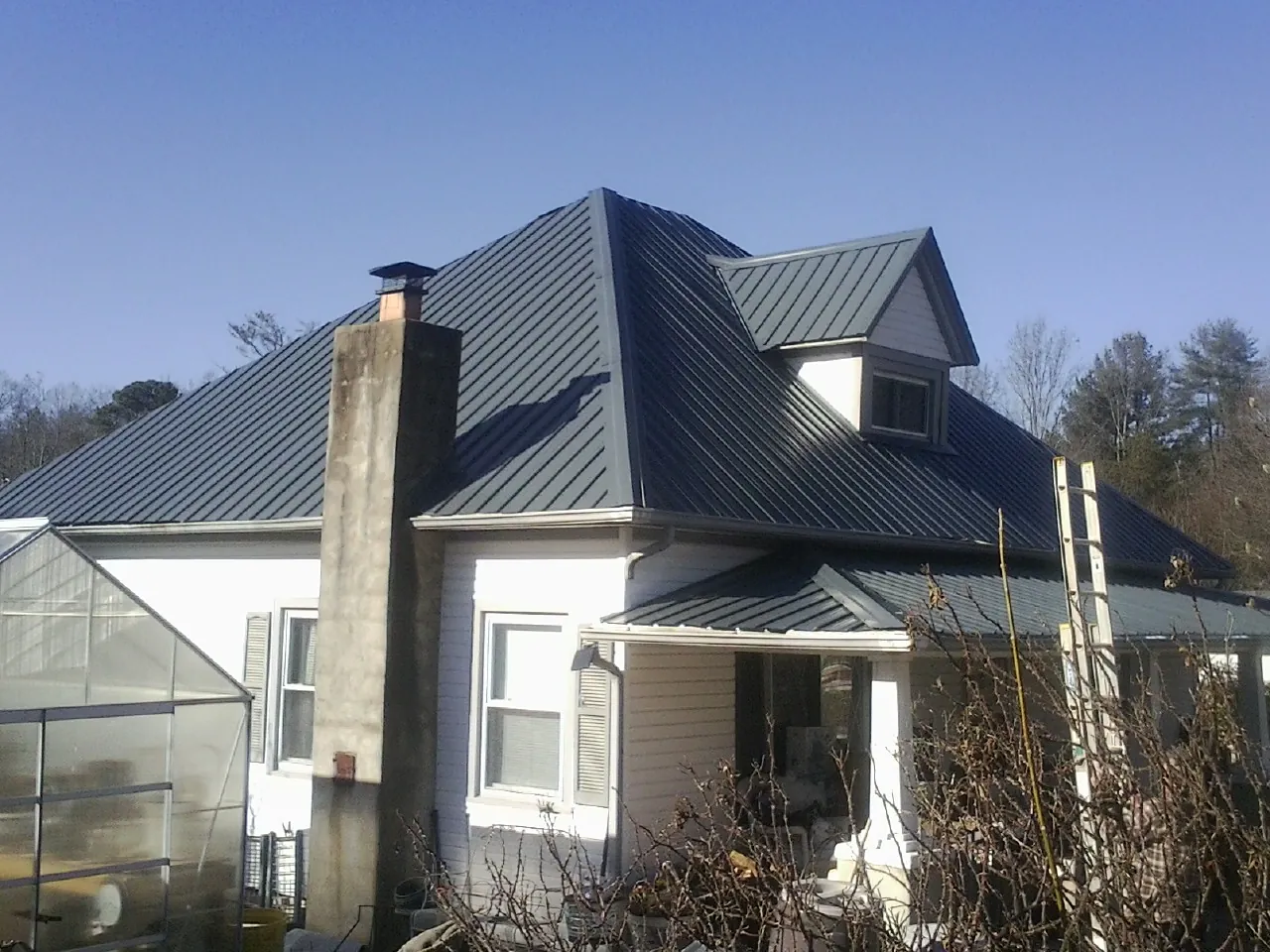 Dark blue standing seam metal roof on a white farmhouse with dormer — Slate & Tile Roof Repair by Roofing Brothers in Pleasant View