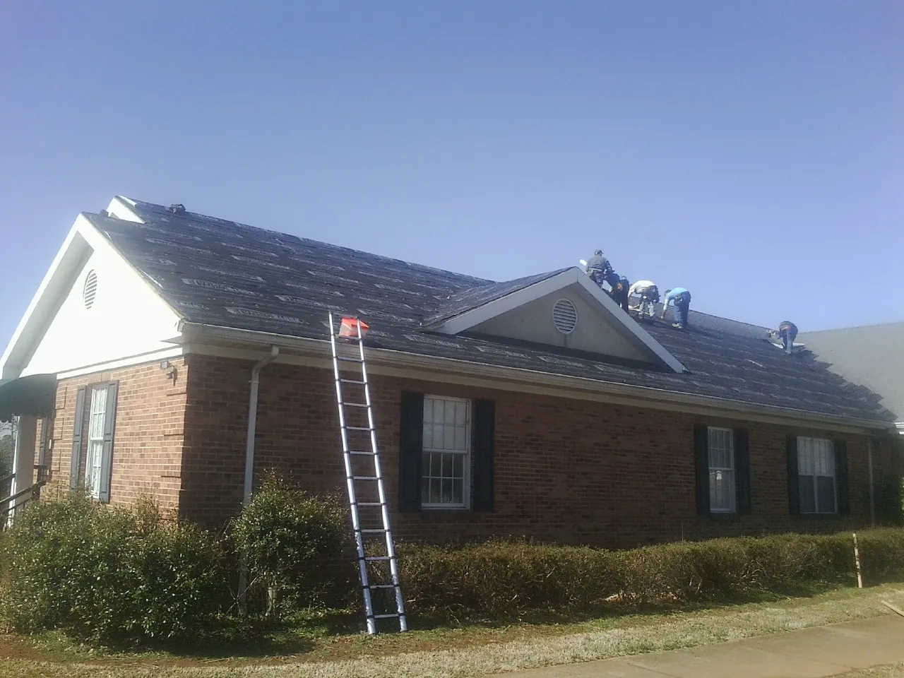 Crew tearing shingles off a brick ranch roof with a ladder set — Metal Roof Repair work by our crew in Pleasant View