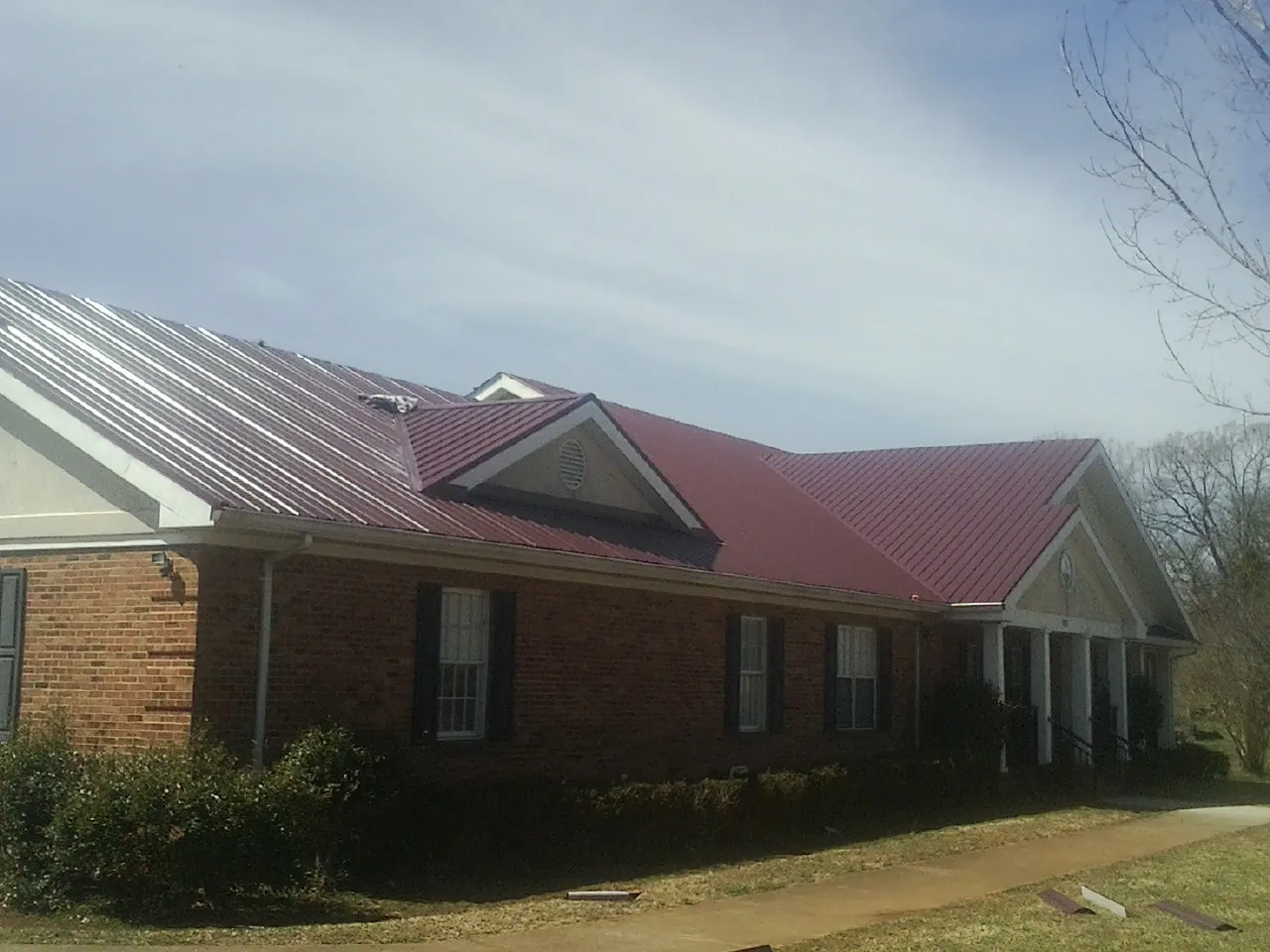 Red metal roof with gabled entries on a long brick building, from a Hail Damage Roof Repair job in Pleasant View