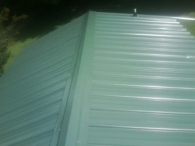 New green metal panels meeting at the ridge of a roof — Flat Roof Repair work by our crew in Pleasant View