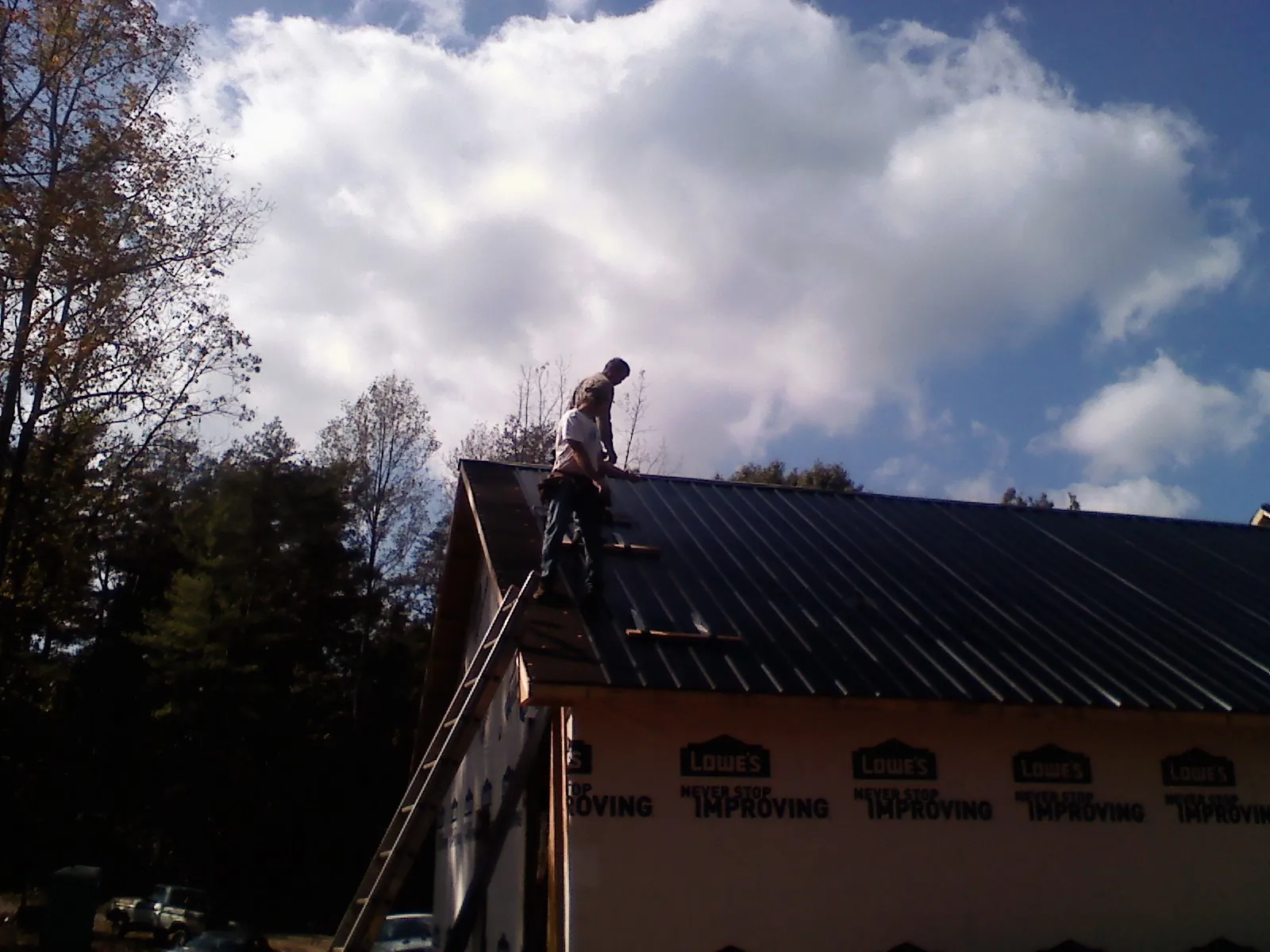 Roofer fastening dark metal panels high against a cloudy sky, from a Roof Inspection job in Pleasant View