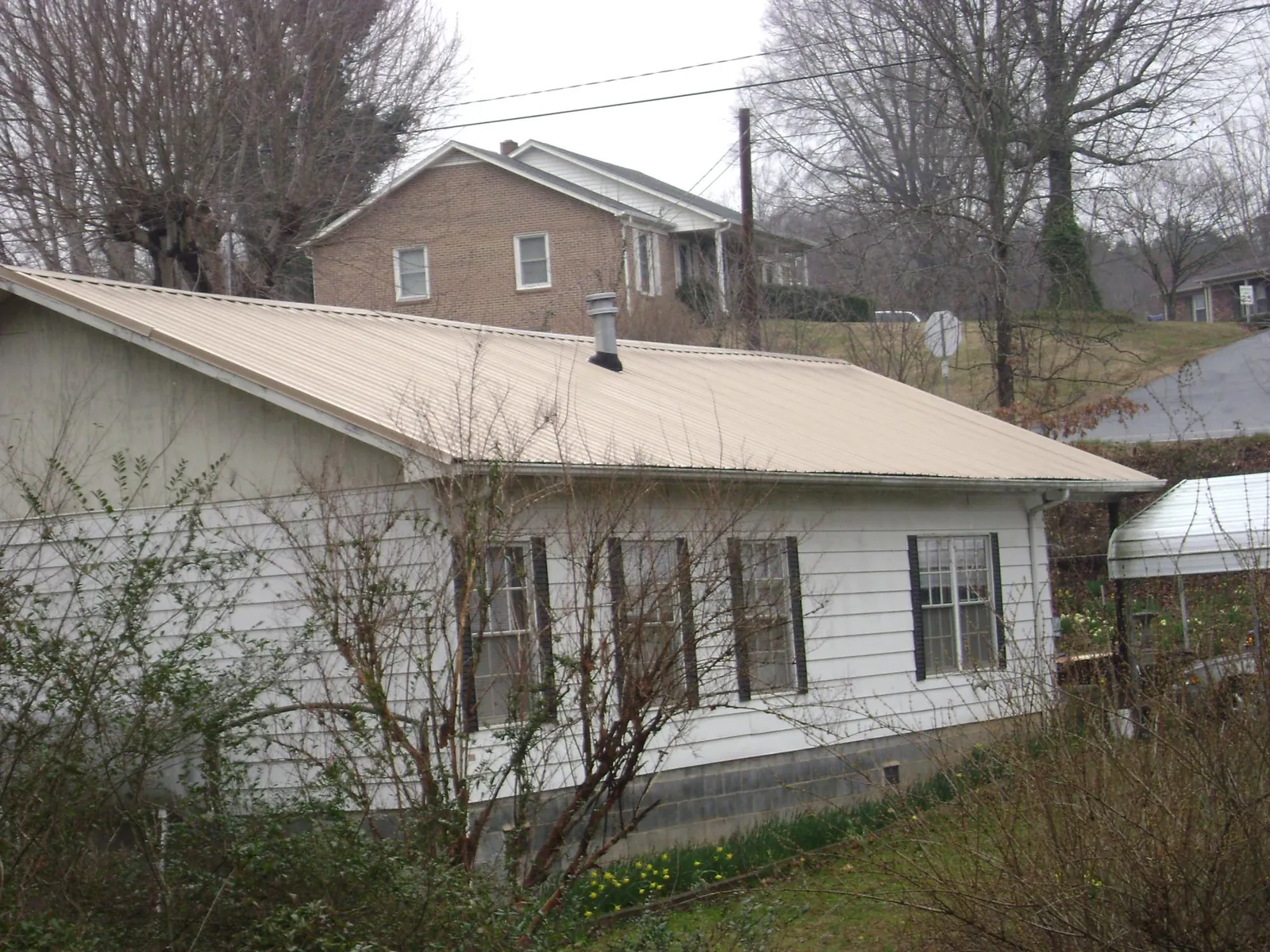 Tan metal roof on a white sided house set into a hillside — Commercial Roofing by Roofing Brothers in Pleasant View