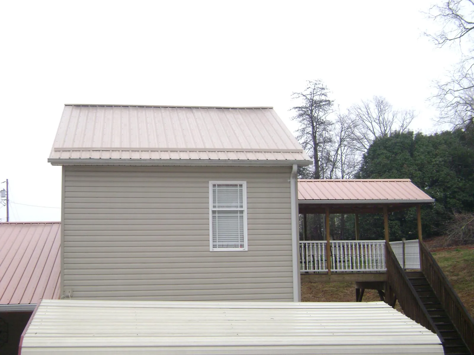 Tan metal roofs on a two story addition and attached porch, from a Roof Replacement job in Pleasant View